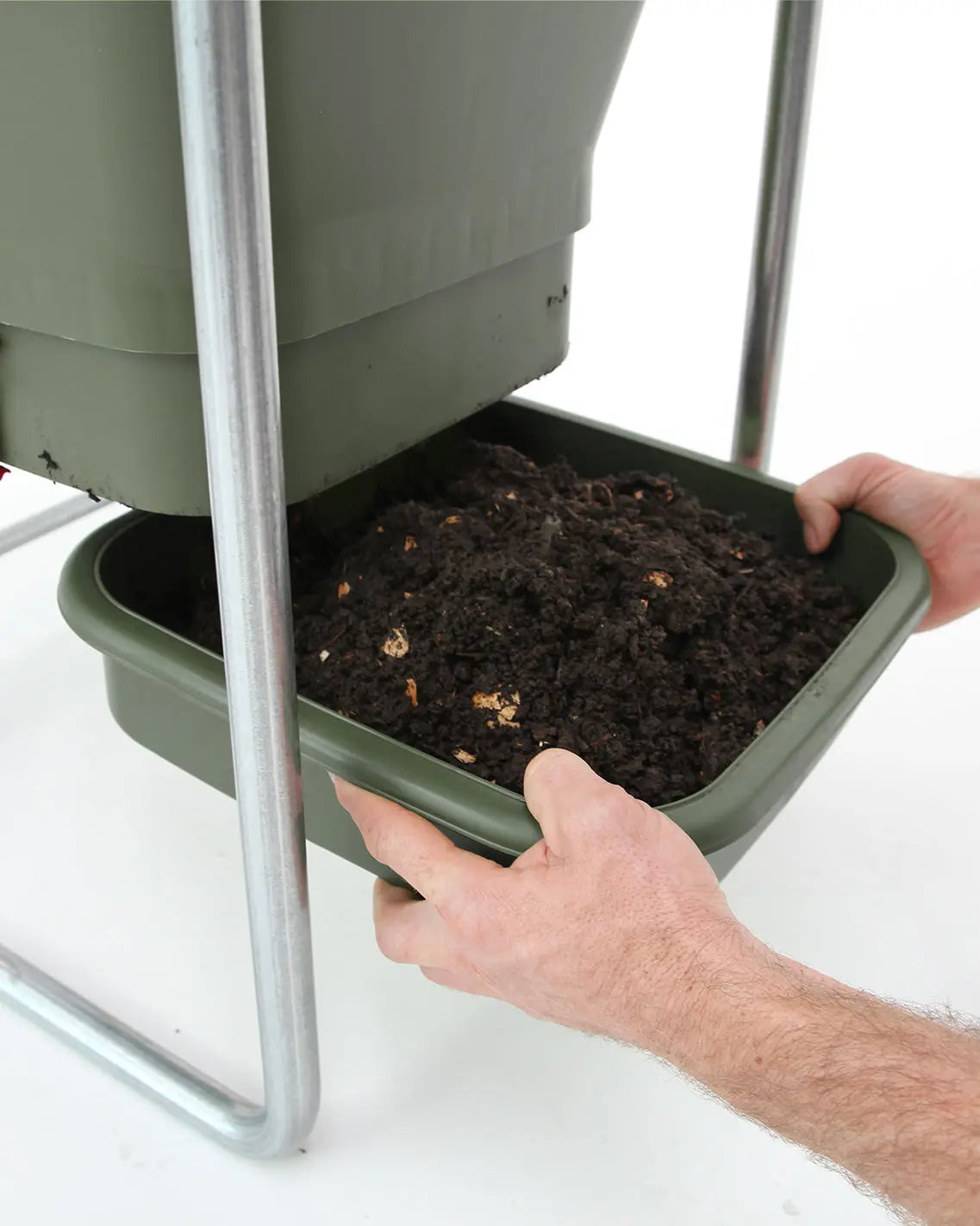 A person slides a green Hungry Bin Continuous Flow Worm Farm tray filled with rich fertilizer from under the raised metal-framed compost bin.