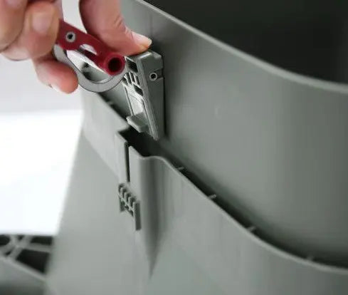 A close-up of a hand using a small red tool to unlock the Hungry Bin Replacement Latch on a green Hungry Bin compost container.